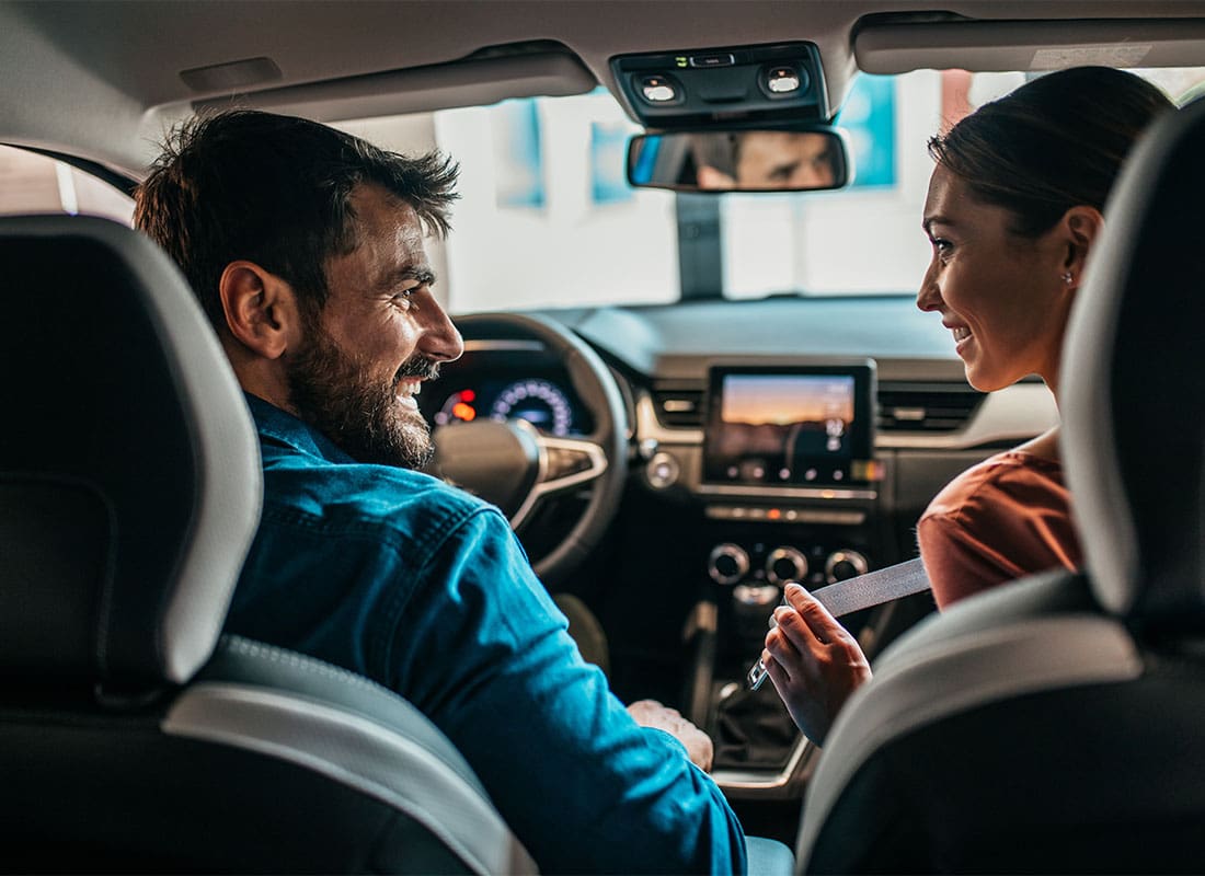 Auto Insurance - Two People in Car Man Driving Smiling at Passenger